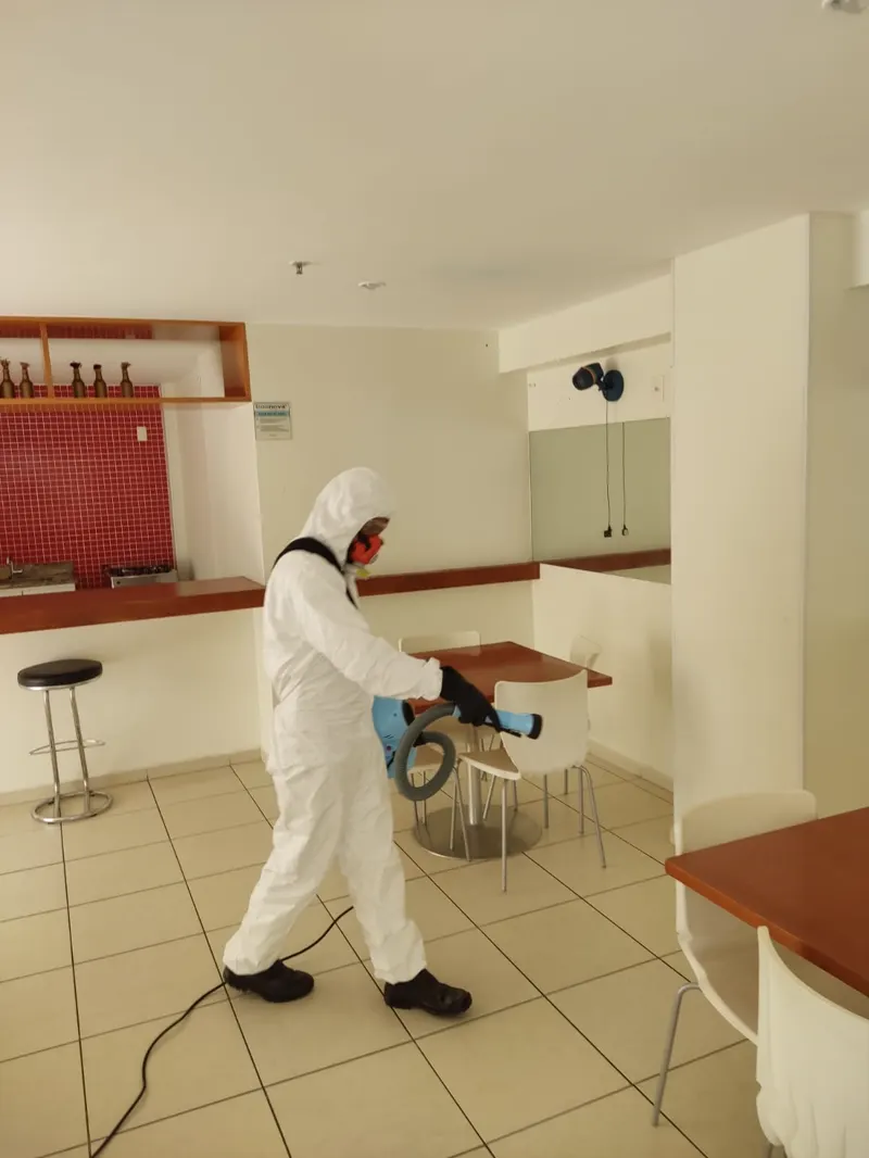 Técnico da Essencial Saúde Ambiental com macacão de proteção aplicando produto no salão de um condomínio