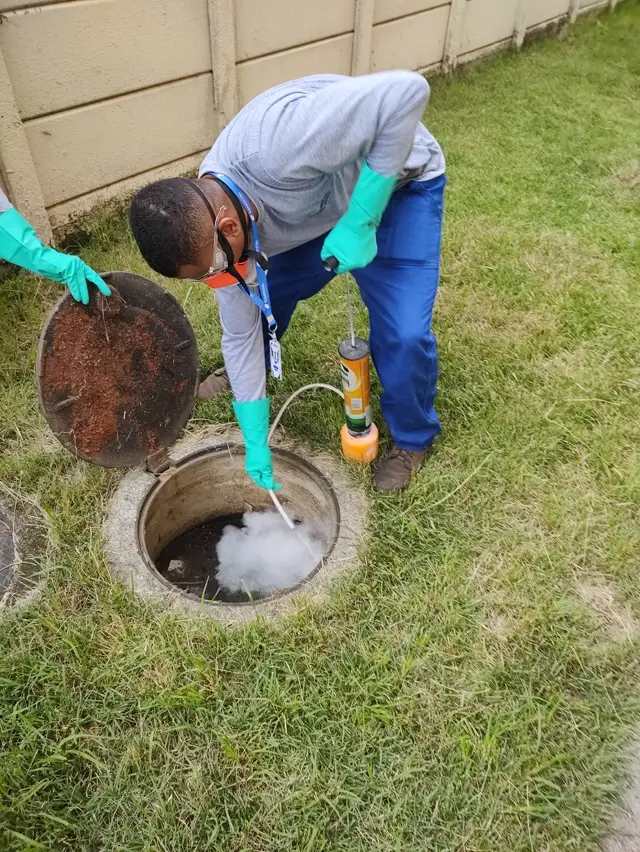 Técnico da Essencial Saúde Ambiental aplicando tratamento contra baratas e ratos na caixa de esgoto